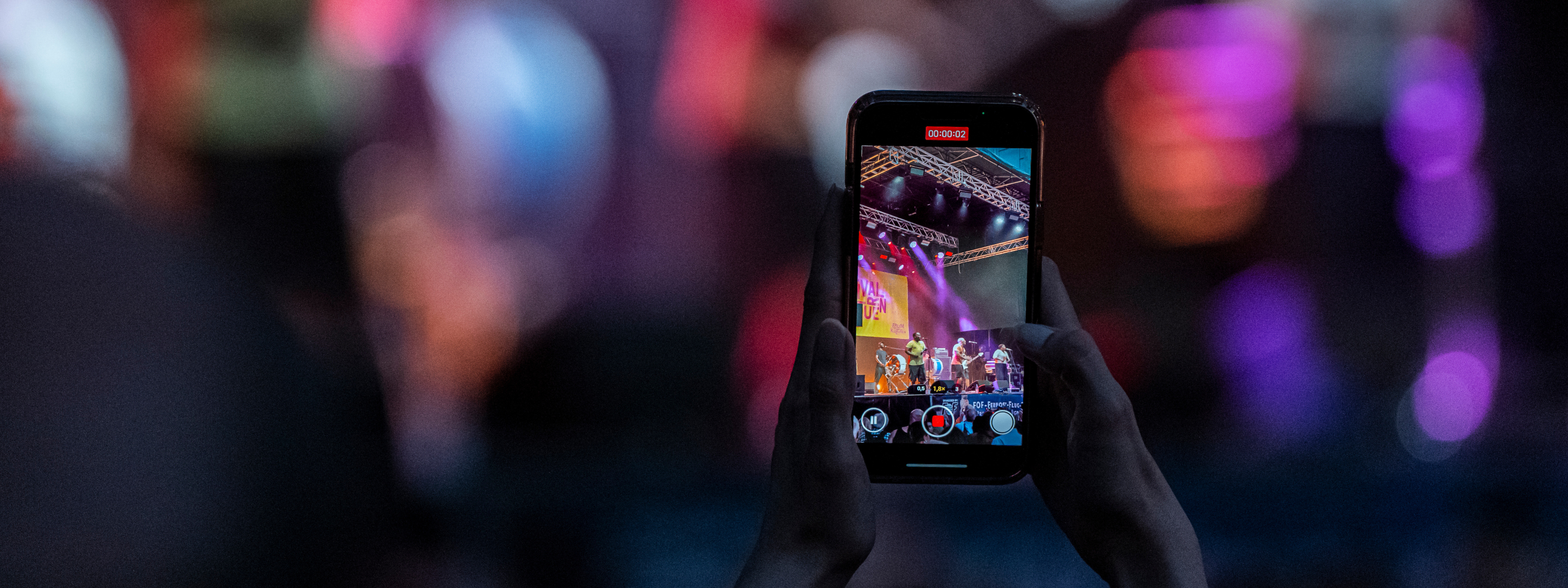 Das Bild zeigt ein Smartphone, das gerade eine Bühnenszene beim Sommerfestival der Kulturen filmt.